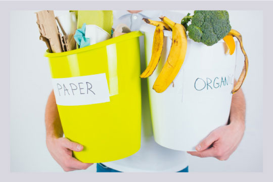 A man standing with two bins of segregated waste labelled paper and organic respectively.